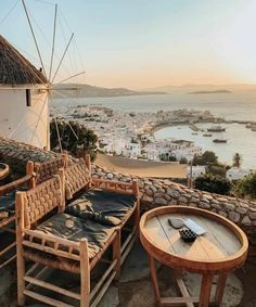 an outdoor patio with wicker furniture overlooking the sea and town in the background at sunset