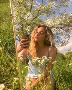 a woman sitting in the grass taking a selfie with her cell phone and looking at it