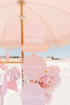 there is a pink umbrella and some signs on the beach with flowers in front of it