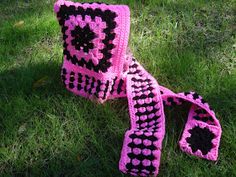 a pink and black crocheted scarf laying on the grass