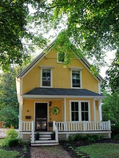 a yellow house with white pickets and trees