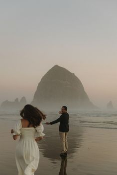 a man and woman walking on the beach with an island in the background at sunset