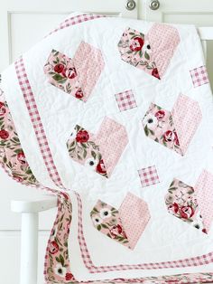 a white quilt with pink and red flowers on it sitting on a chair next to a wall