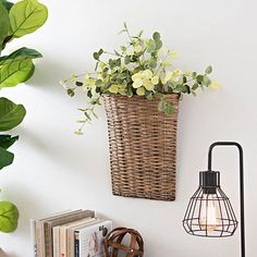 a basket with flowers hanging on the wall next to a lamp and bookshelf