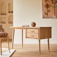 a wooden desk sitting next to a chair on top of a hard wood floor in front of a white wall