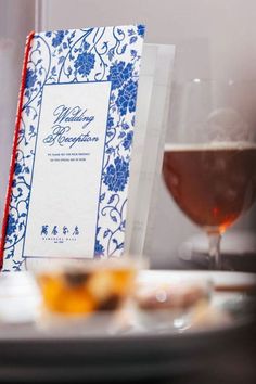 a table topped with a glass of wine and a menu next to a plate filled with food