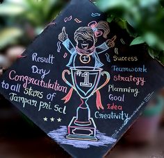 a black graduation cap with writing on it and a drawing of a woman holding a trophy