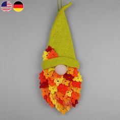 a crocheted gnome hat hanging on the wall with flowers around it's face