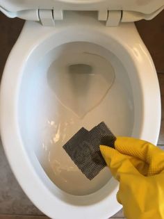 a person in yellow gloves cleaning a white toilet with a microfiber and cloth