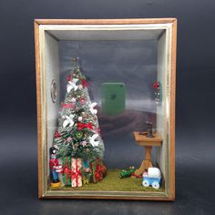 a miniature christmas tree in a case with toys around it and a phone on the table