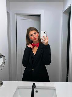 a woman taking a selfie in front of a bathroom mirror wearing a red bow tie