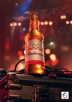 a bottle of budweiser beer sitting on top of a piece of luggage with lights in the background