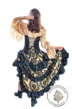 Wild West Skirt: Gold and Black with Silver Ruffles The Gold and Black wild west skirt with black ruffles is shown here with a silver fancy chemise and a black corset. The new Wild West skirt is ruffle heaven with nine ruffles per skirt. The skirt is short in the front, and falls above the knees. It is full length in the back with two rows of double ruffles, and a single row in the center. This skirt features a solid color ruffle that coordinates with the fabric, and some skirts will have multip Saloon Outfits, Victorian Pirate, Western Steampunk, West World, Steampunk Victorian, Cowboy Party, Black Corset, Women's Costumes, Black Ruffle