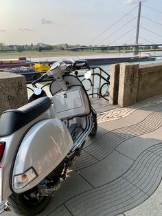 a motor scooter parked next to a concrete wall near the water with a bridge in the background