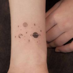 a small wrist tattoo with planets and stars on the left side of the arm,