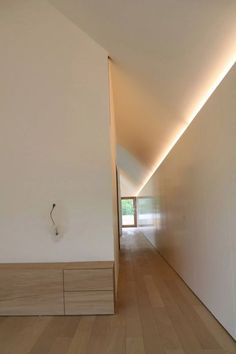 an empty hallway with white walls and wooden flooring is lit by recessed lighting