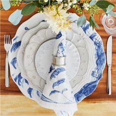 a blue and white place setting on a wooden table with flowers in the centerpiece