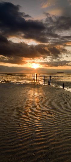 the sun is setting over the ocean with some wooden posts sticking out of the water