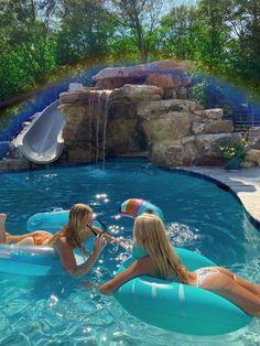 two women are in an inflatable pool with a waterfall and slide behind them