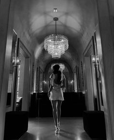 a woman is walking down the hall with chandelier hanging from the ceiling in front of her