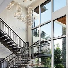 a staircase with chandelier hanging from it's side in front of large windows