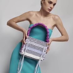 a woman in a blue dress holding a white and purple handbag on her shoulder