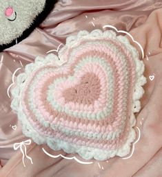 a crocheted heart on a pink blanket with a teddy bear in the background