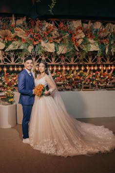 a bride and groom posing for a photo in front of a floral wall with candles