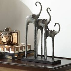 three metal sculptures sitting on top of a wooden table next to a camera and box