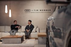 two men sitting on couches in front of a wall with an audi logo behind them