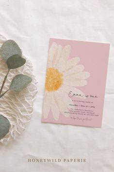 a pink and yellow flower on top of a white table cloth next to a card