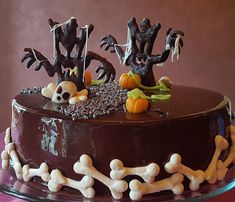 a chocolate cake decorated with halloween decorations and bones on a glass platter in front of a pink wall