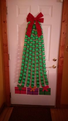 a christmas tree made out of legos is hanging on the front door with a red bow