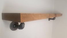 a wooden shelf mounted to the side of a wall with two pipe holders on it