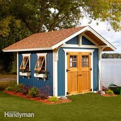 a small blue and brown shed sitting on top of a lush green field next to a body of water