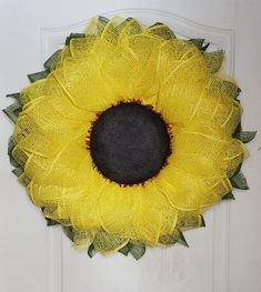 a yellow sunflower is hanging on the front door with green leaves and mesh around it