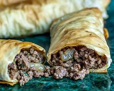 there are two burritos cut in half on the counter top and one has meat inside