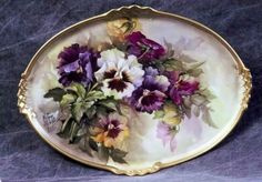 a plate with flowers painted on it sitting on a purple tableclothed surface,