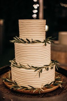 a three tiered white cake with green leaves on the top is sitting on a wooden table