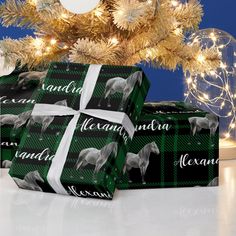 two presents wrapped in black and white wrapping paper with horses on them, under a christmas tree