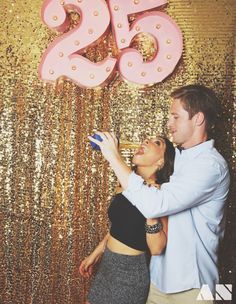 a man and woman standing next to each other in front of a gold sequin backdrop