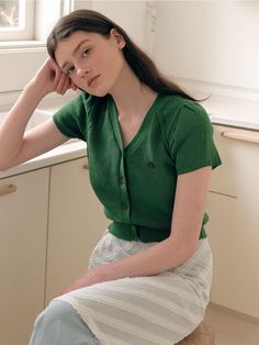 a young woman sitting on top of a stool in a kitchen next to a window