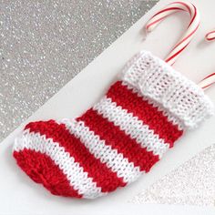 a red and white knitted stocking with candy canes next to it on a table