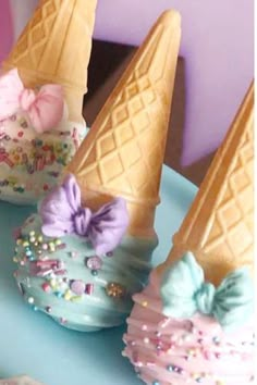 three ice cream cones decorated with bows and sprinkles on a blue plate