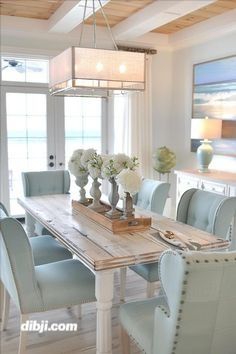 a dining room table with blue chairs and white flowers in vases on the end