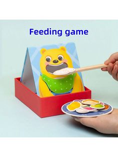 a hand holding a wooden spoon over a plate with food on it and the words feeding game