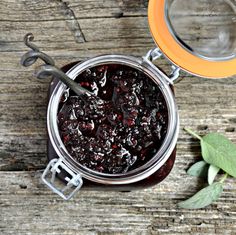 a glass jar filled with jam next to a green leaf on top of a wooden table