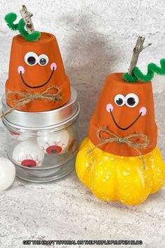 two paper pumpkins with googly eyes sitting next to an egg in a tin