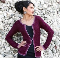 a woman standing in front of rocks wearing a purple cardigan and black dress with her hands on her hips