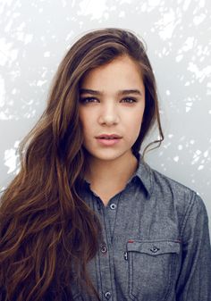 a woman with long hair standing in front of a white wall and looking at the camera